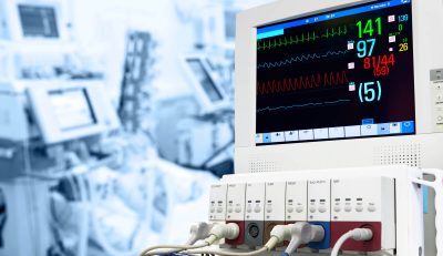 תמונת נושא של המאמר על מכירת ציוד רפואי המציגה מוניטור רפואי להצגת סימנים חיוניים בחדר טיפול נמרץ עם תצוגת דופק לחץ דם וחמצן המכשיר מחובר למטופל מטושטש ברקע הכחול.